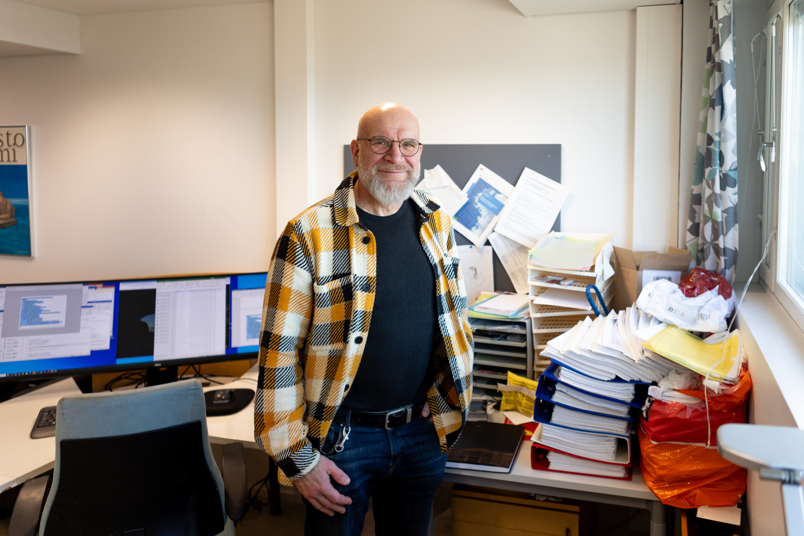 Petri Näätänen seisoo työpöytänsä äärellä, joka tosiaan näyttää siltä että töitä on tehty ja hymyilee. 