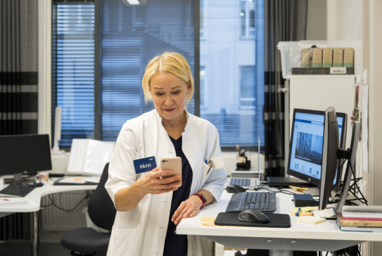 Lääkäri Lehtovirta seisoo työhuoneensa pöydän äärellä ja katsoo kädessään olevaa puhelinta, jossa on Haiku-sovellus auki. Puolikuva
